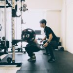 パーソナルジムでバーベルスクワットのフォーム指導を受ける様子。筋力とパワーを高め「行動を起こす能力」を改善。