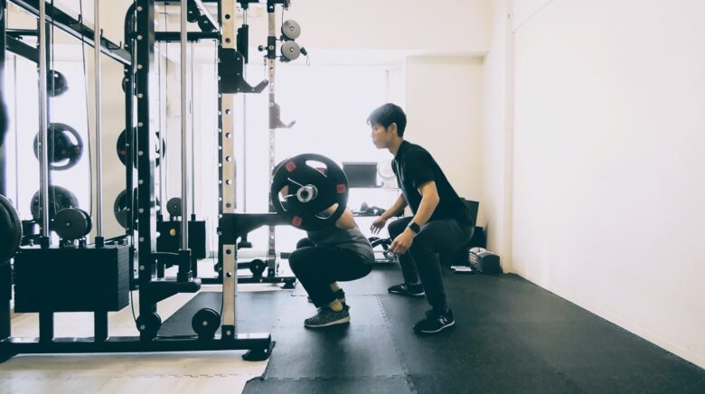 パーソナルジムでバーベルスクワットのフォーム指導を受ける様子。筋力とパワーを高め「行動を起こす能力」を改善。