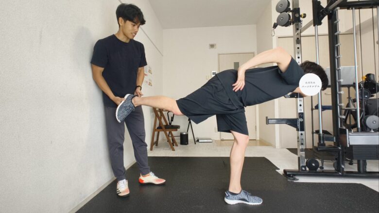 金山のパーソナルジムで、トレーナーが男性のシングルレッグルーマニアンデッドリフトのフォームをサポートする様子。