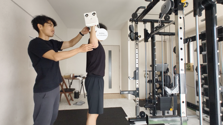 金山のパーソナルジムでのトレーニング風景。トレーナーがお客様の横につき、肩のトレーニングフォームを丁寧に指導している。