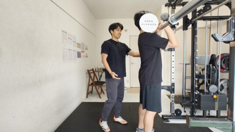 金山にあるパーソナルジムのトレーナーが、バーベルを使ったフロントスクワットの正しいフォームを丁寧に指導している様子。初心者でも安全にトレーニングができるようサポートしています。