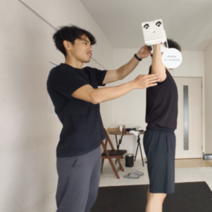 金山のパーソナルジムでのトレーニング風景。トレーナーがお客様の横につき、肩のトレーニングフォームを丁寧に指導している。