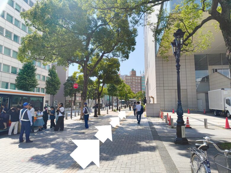 木々が並ぶ金山駅周辺の広い歩道を直進する様子。白い矢印で進行方向を指示。