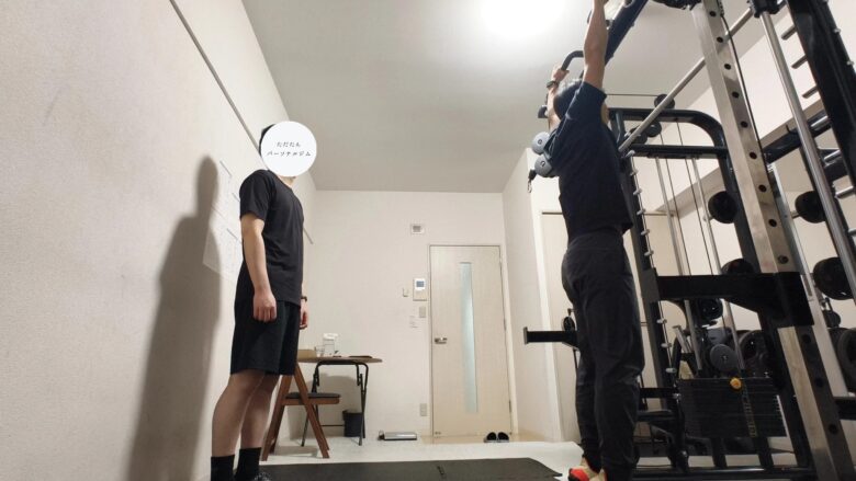 マンツーマンで懸垂(チンニング)のフォームをチェックするトレーナーと、マシンの前で準備する利用者の様子。