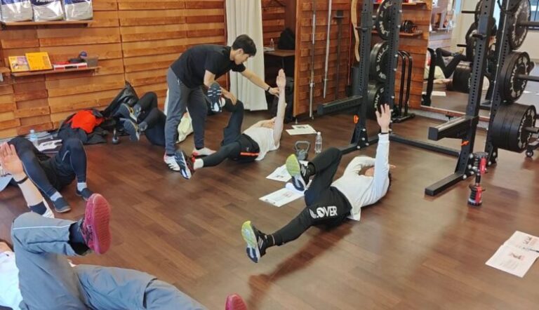 金山のパーソナルジム「ただたん」代表が、技術セミナーにて、参加者の足の角度や体幹の固定を細かく修正しながら、デッドバグの正しいフォームを直接指導している様子。